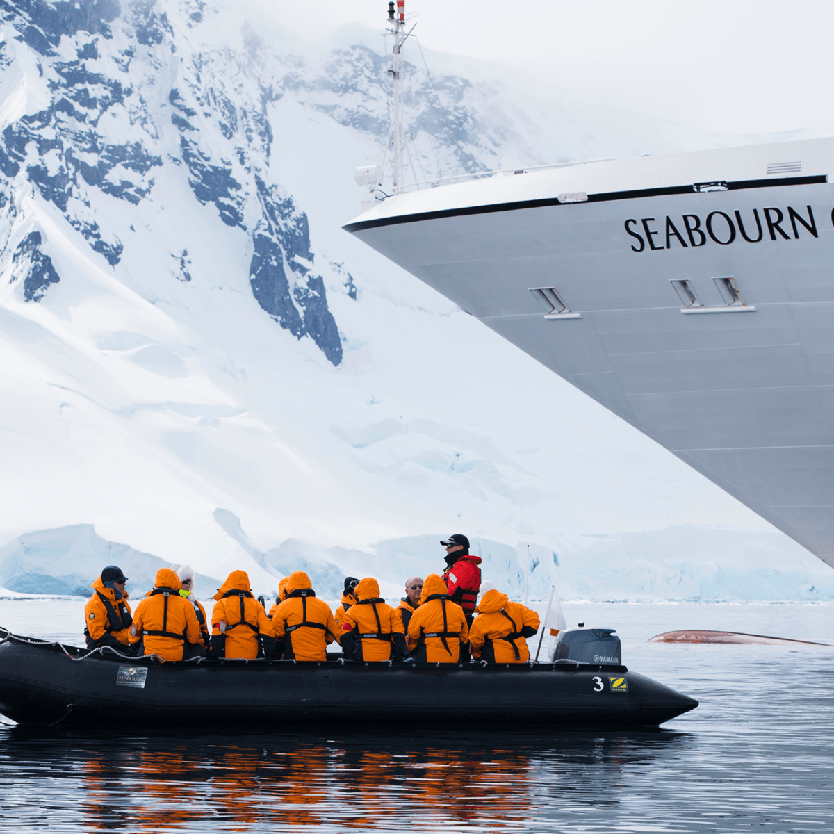 The bow of a cruise ship in the arctic, with passengers in an expedition vessel in front of it.